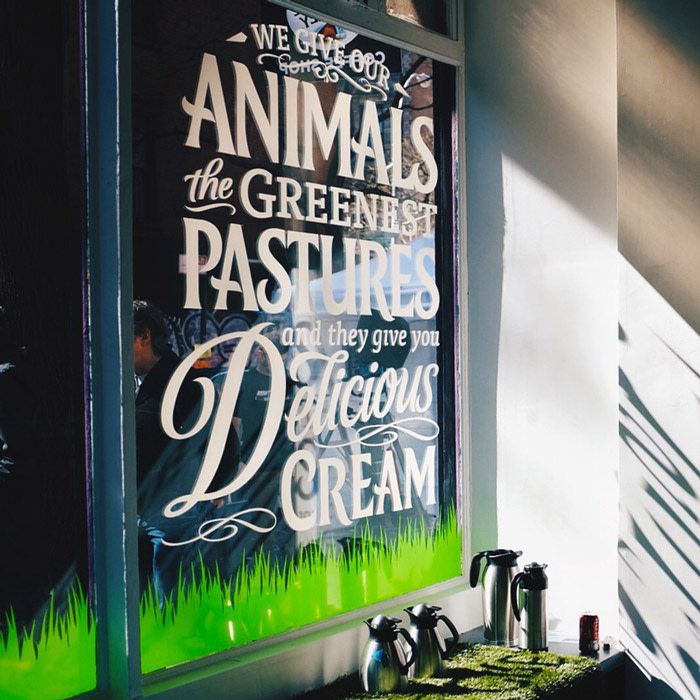 a window for a coffee shop with the words on it, "we give our animals the greenest pastures and they give you delicious cream"