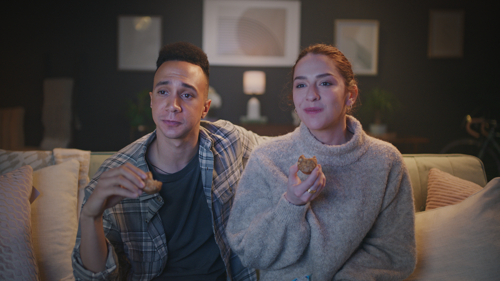 Man and woman sit on a couch in a home while watching television eating bobo's