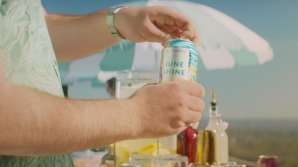 close shot of man holding June Shine can with the beach in the background