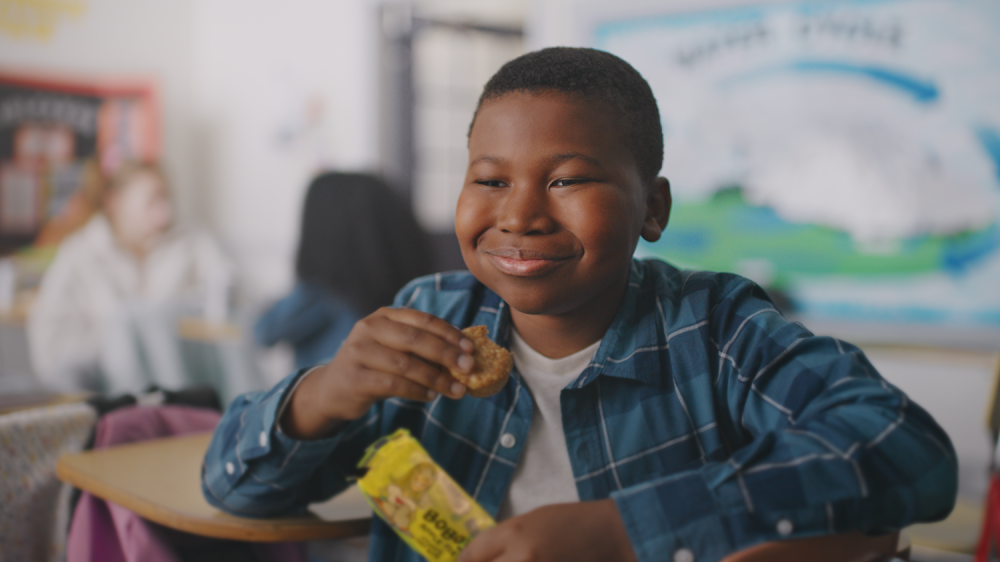 Child eats Bobo bar in classroom while sitting at a desk