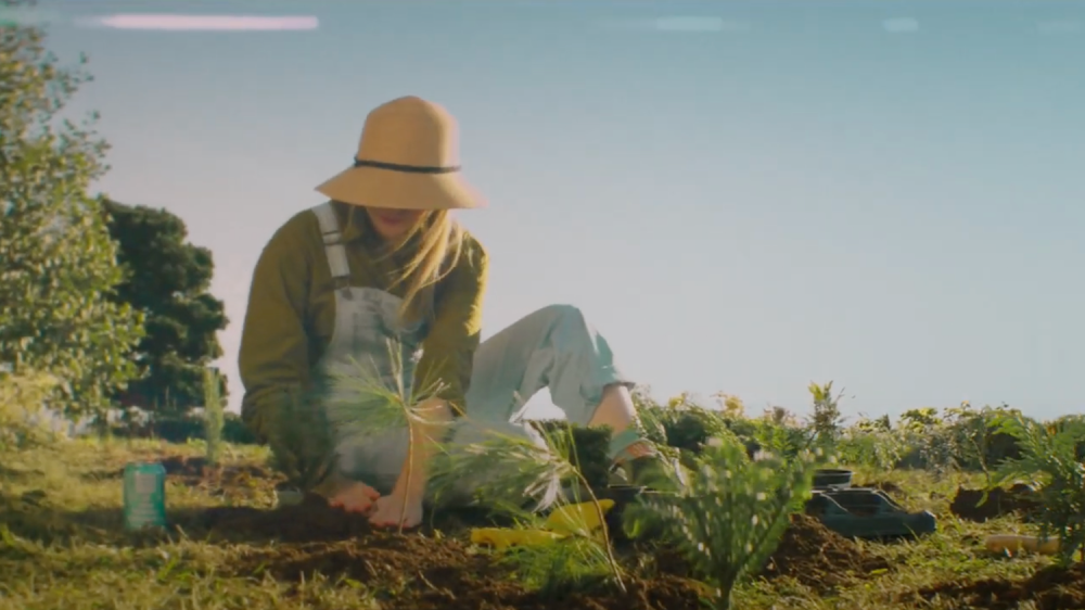 Woman in overalls sits on the ground planting with her hands in the dirt