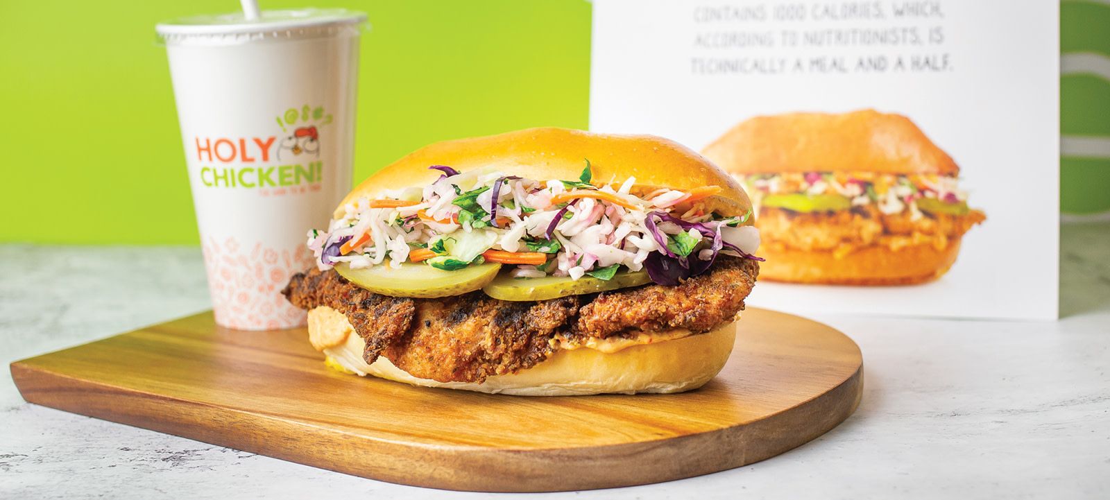 a chicken sandwich and drink from holy chicken sits on top of a wooden cutting board