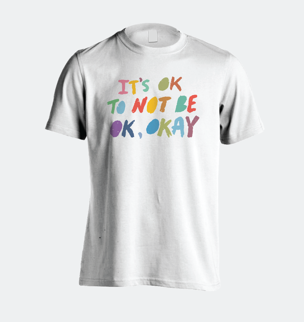 A white shirt with a crayon looking multicolored type that reads, "It's ok to not be ok, okay"