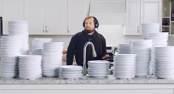 A man in a kitchen wearing headphones and with stacks of plates surrounding him