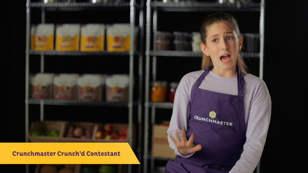 Girl Child chef contestant is interviewed in a straight on shot with a shelf of ingredients in the background