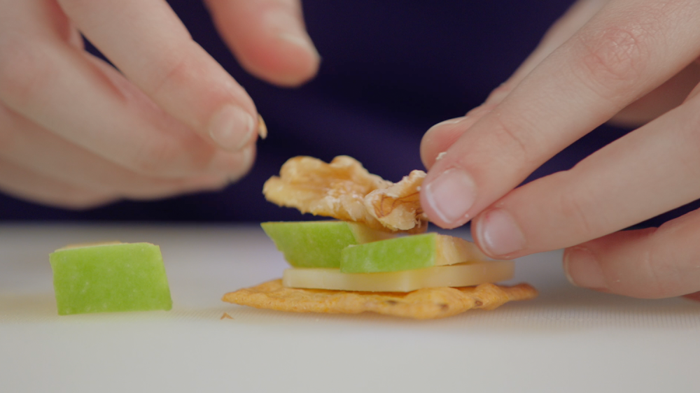 Close up shot of hands putting cheese apples and walnut on a cracker