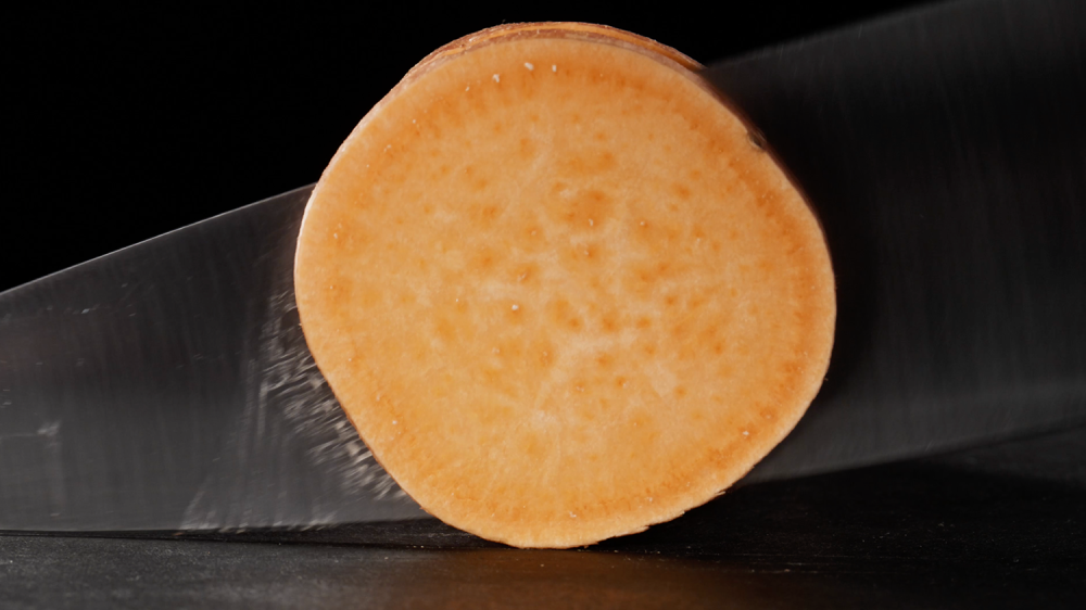 A side angle of a knife cutting through a sweet potato