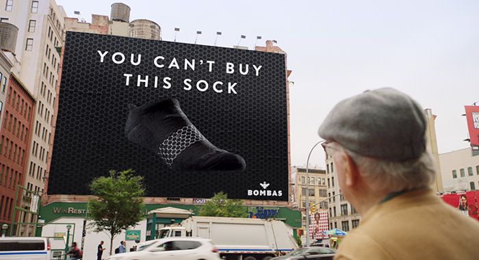 An older man in a city looks up to an advertisement with a sock and words, " you can't buy this sock" on it