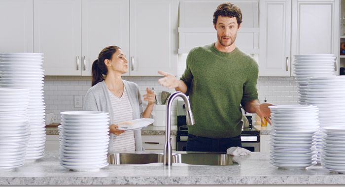 A man and a woman in a kitchen with a sink in front of them and many tall stacks of plates