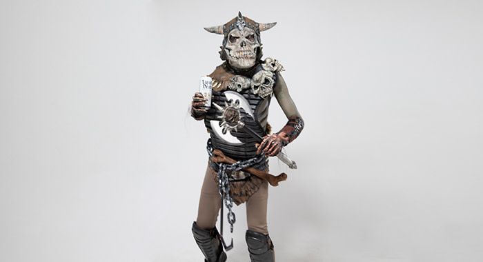 A person in a monster costume holds a white liquid death in their right hand and a double sided axe in the other hand