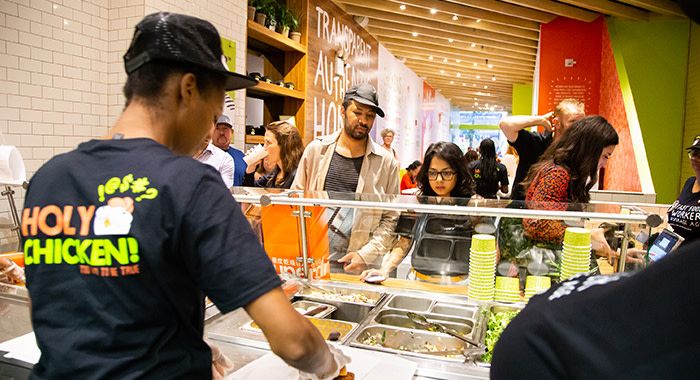 a shot from behind a worker at holy chicken scooping the food while customers watch