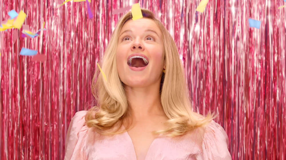 Blond haired girl looks up with her mouth open at confetti falling from the ceiling