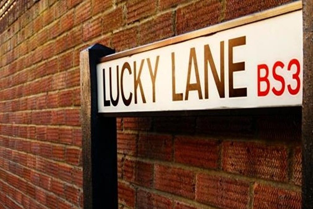 A street name sign for Lucky Lane against a brick wall