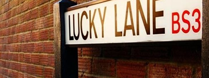 A street name sign for Lucky Lane against a brick wall