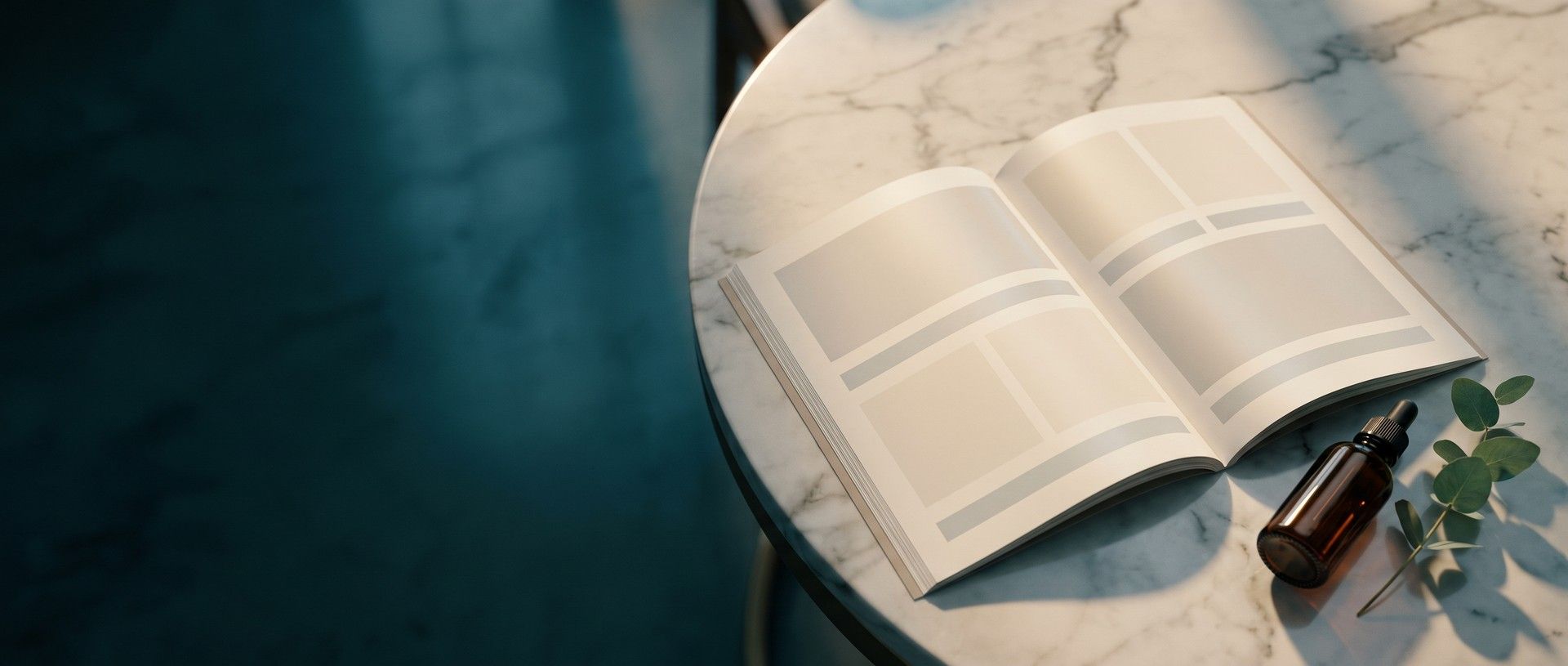 An open brochure with blank photo panels lying on a white marble consultation table in window light, an amber dropper bottle and a eucalyptus sprig beside it