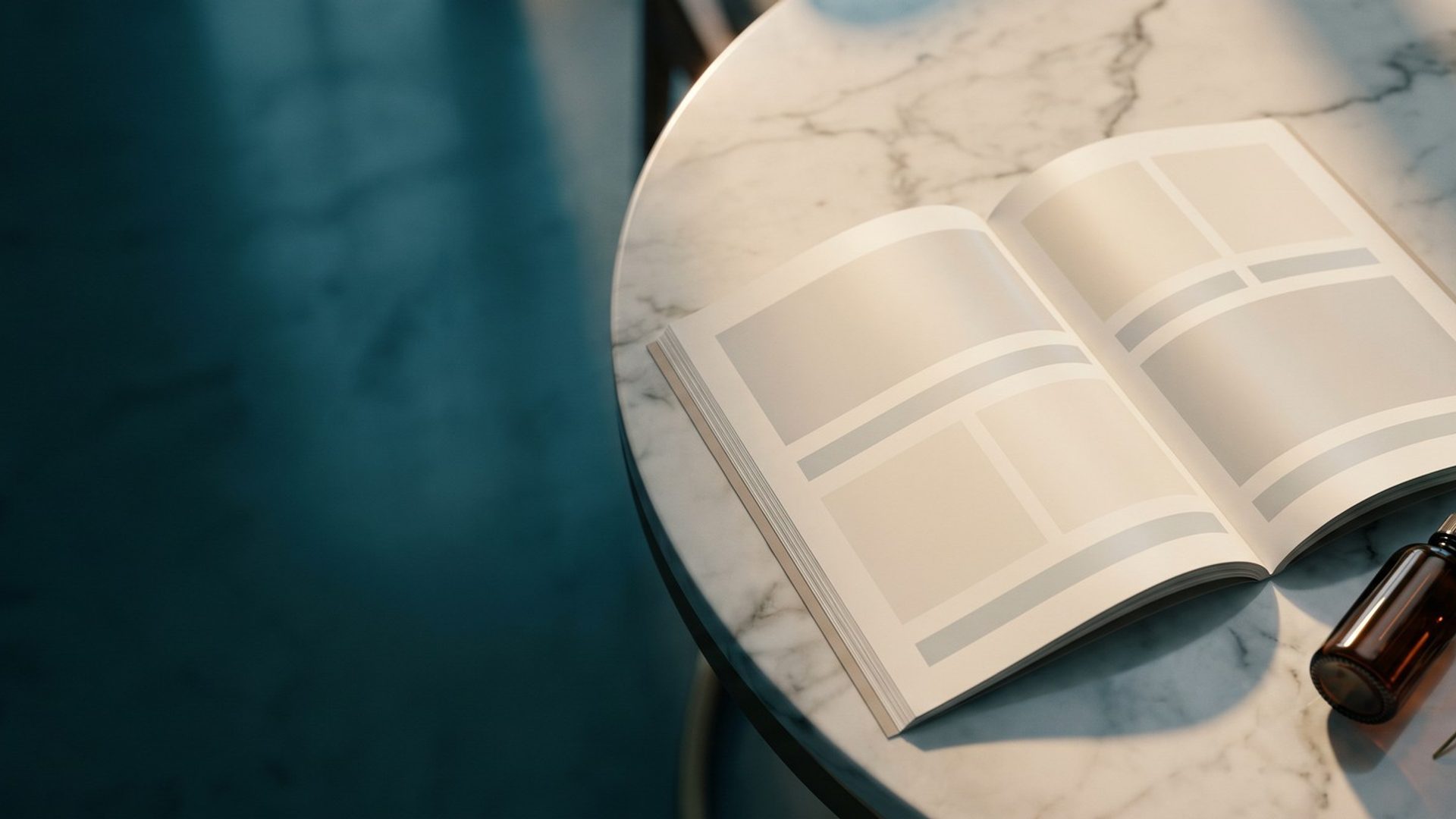 An open brochure with blank photo panels lying on a white marble consultation table in window light, an amber dropper bottle and a eucalyptus sprig beside it