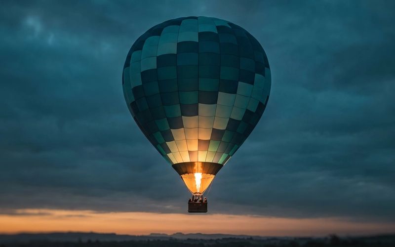 A single hot-air balloon rising steadily at dusk, lifted by a controlled amber burner flame against a deep teal sky - scaling on the fuel you feed it, under control.