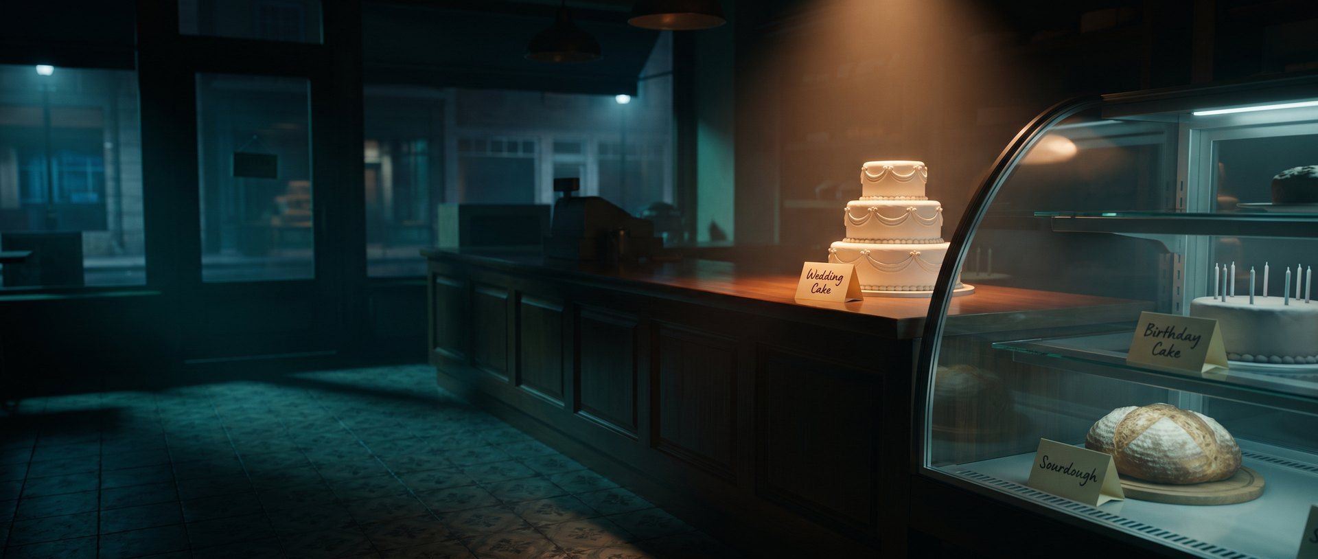 A bakery display case at night with a tiered wedding cake, a birthday cake and a sourdough loaf, each with its own small handwritten label card, the wedding cake and its card lit warm amber