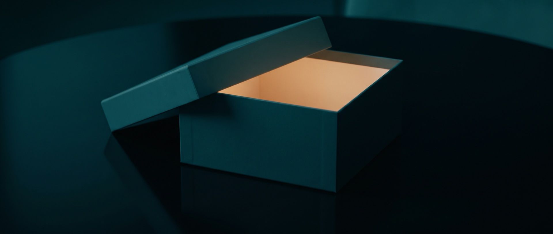 A dark teal box with its lid lifted and warm amber light glowing from inside, on a dark table.