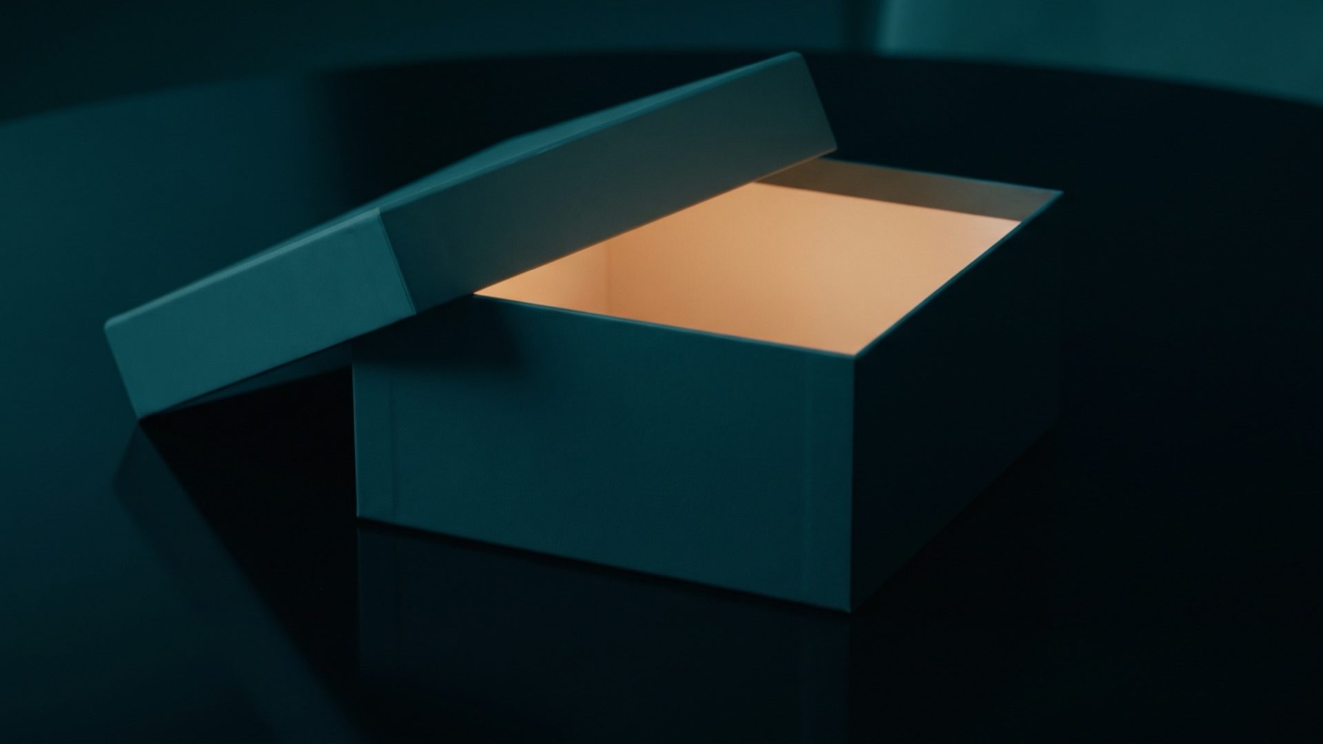 A dark teal box with its lid lifted and warm amber light glowing from inside, on a dark table.
