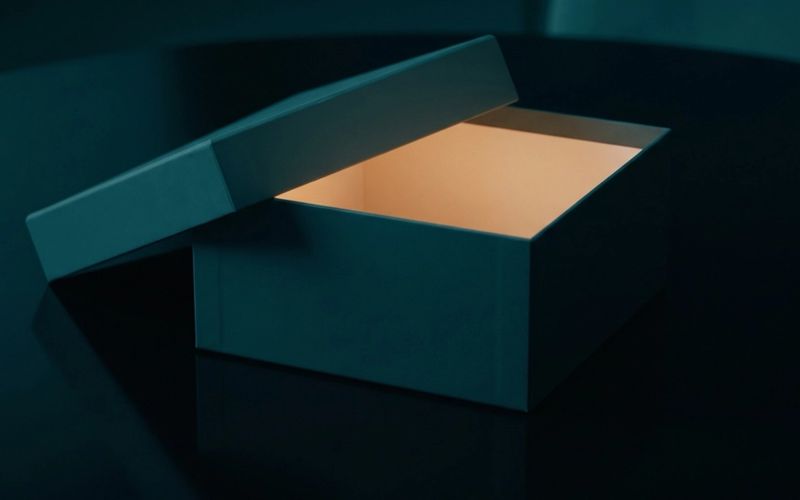 A dark teal box with its lid lifted and warm amber light glowing from inside, on a dark table.