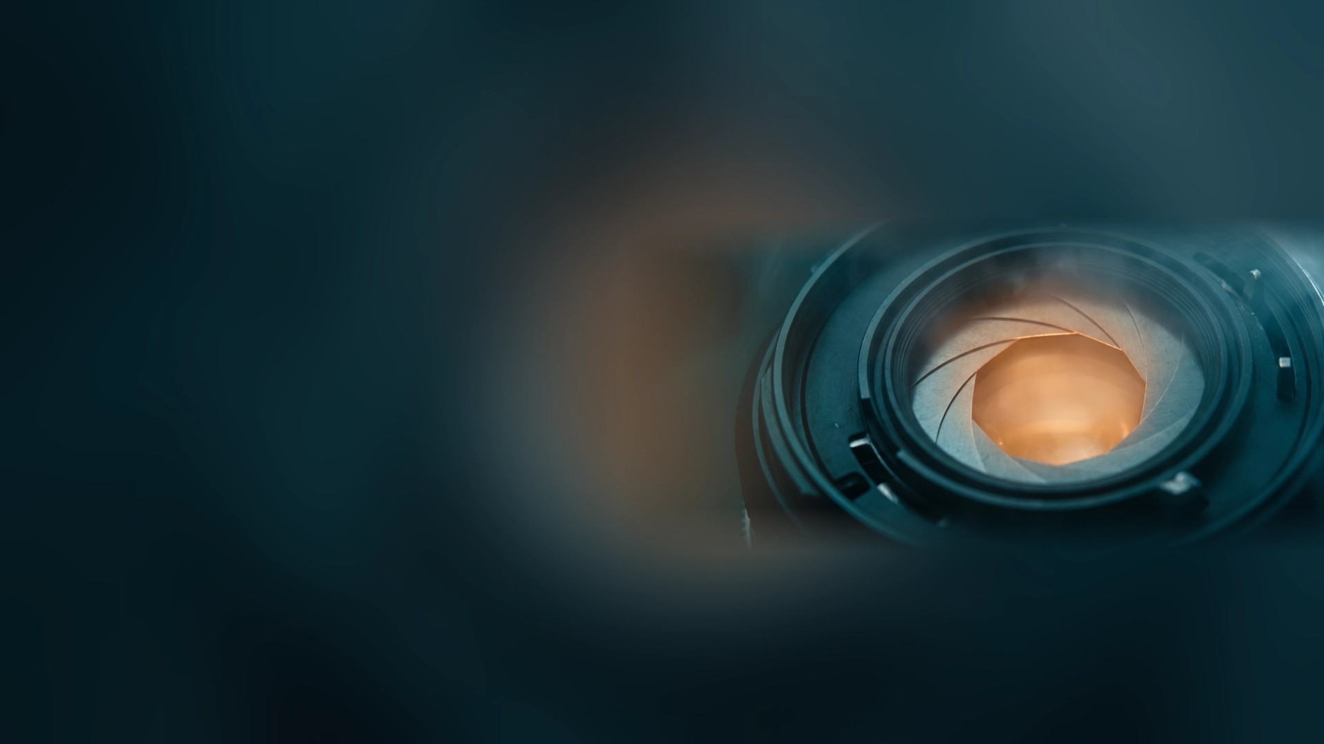 A camera lens with its aperture blades partly closed, glowing amber inside