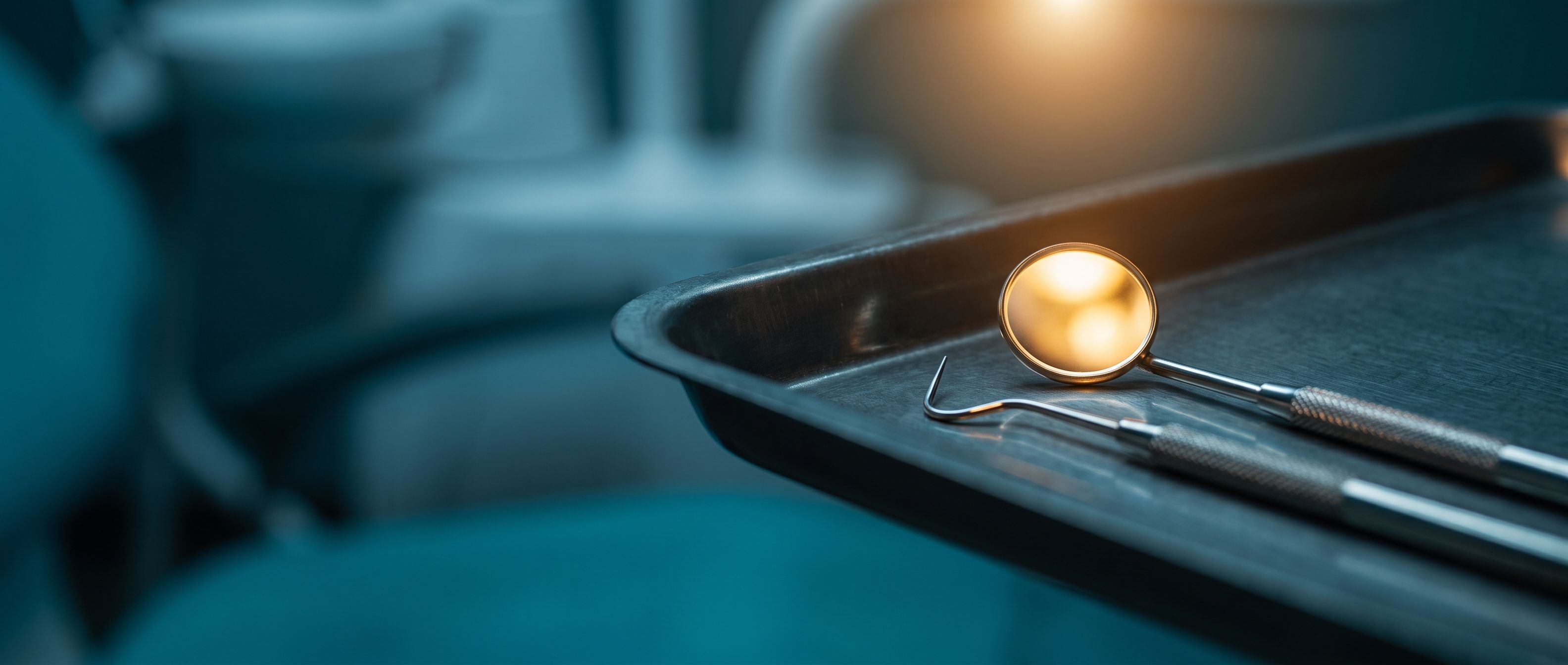 A dental mirror and explorer on a steel instrument tray, the mirror catching warm amber light