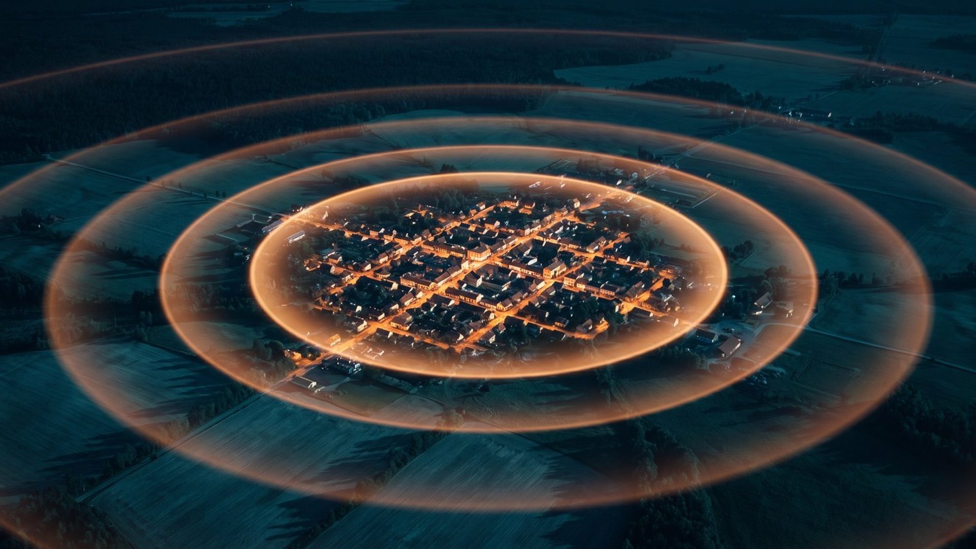 An aerial night view of a small town, its lit streets bright at the center, with concentric rings spreading outward across dark farmland and fading as they travel away from it.