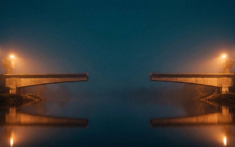 An unfinished road bridge at night, its two halves reaching in from either bank and stopping short of meeting above dark water