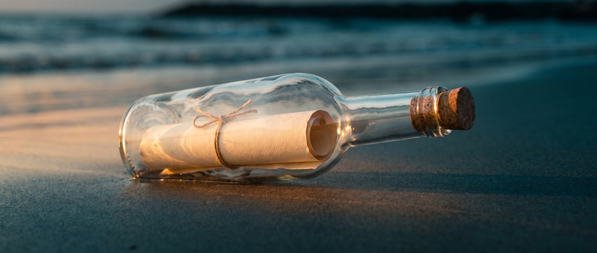 A corked glass bottle on a shoreline at dawn with a rolled paper note still sealed inside, unread