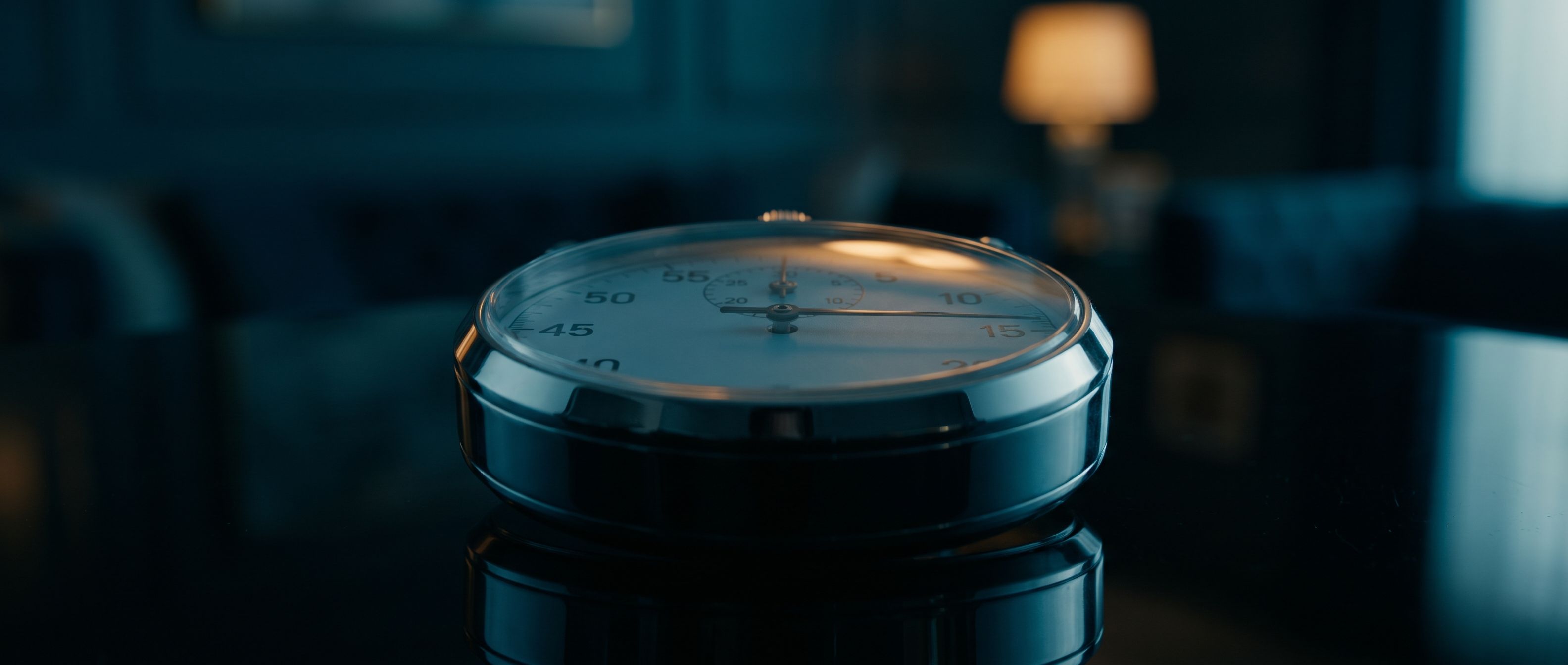 A polished chrome stopwatch on a dark reflective surface, its second hand frozen just past the three-second mark.