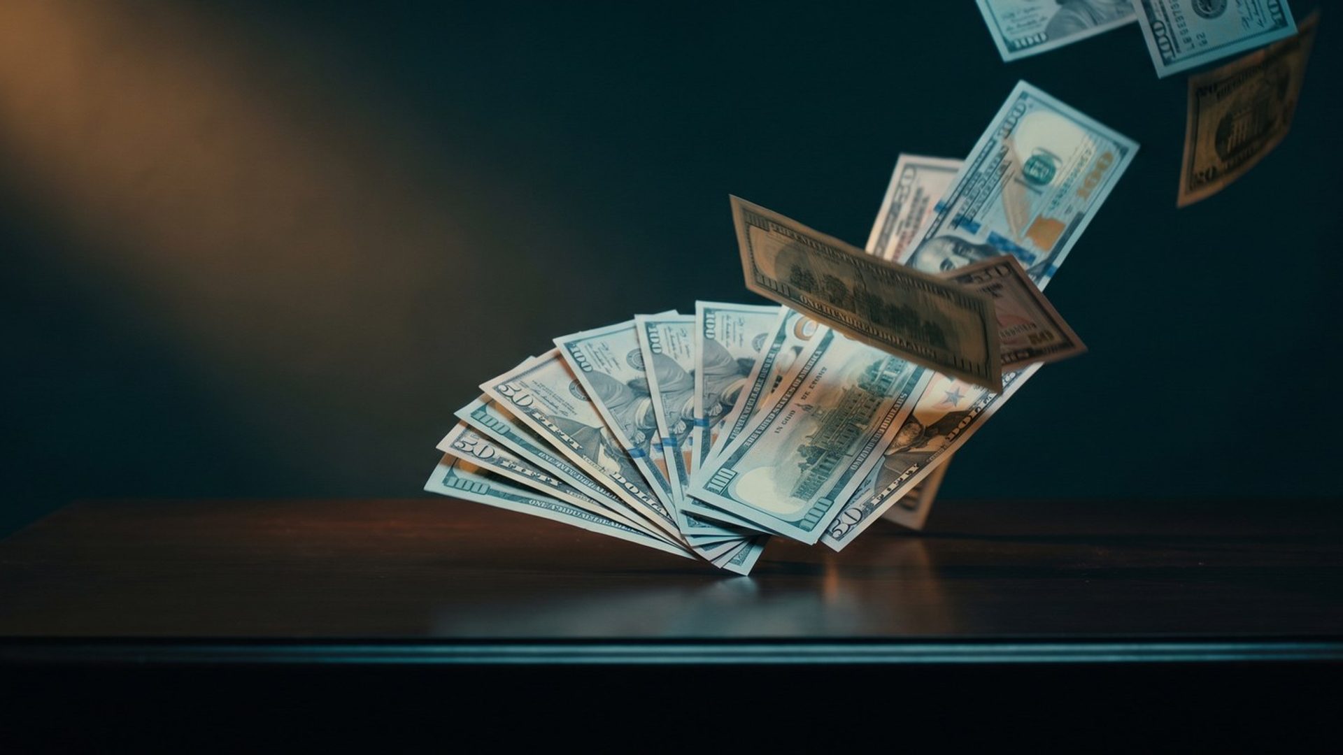Banknotes lifting off a dark desk and scattering into the air