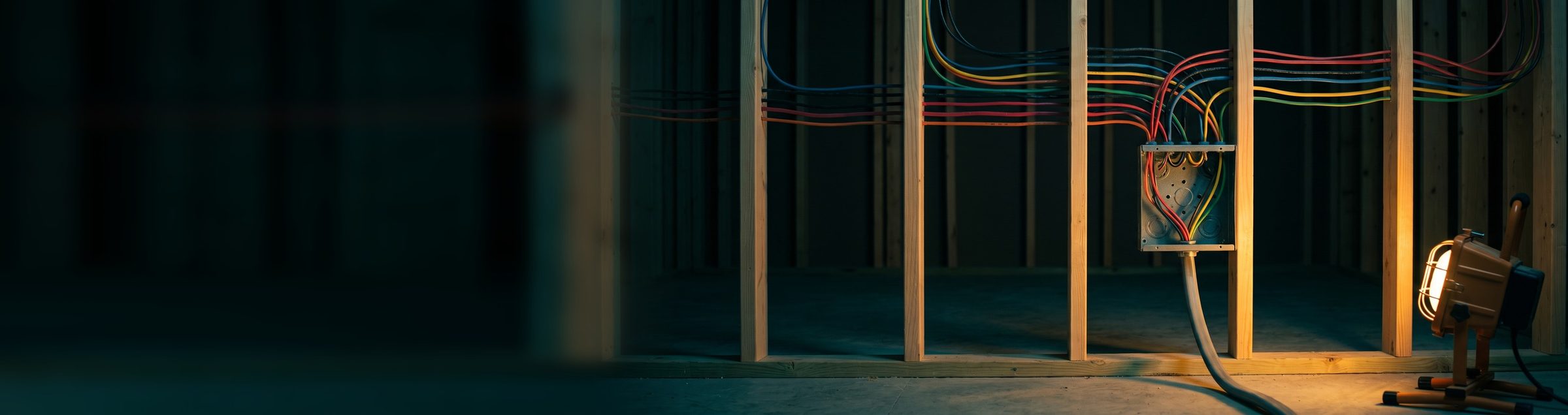 One thick gray cable rising from the floor into an open metal junction box on an unfinished stud wall, with dozens of colored wires spreading out of it across the studs