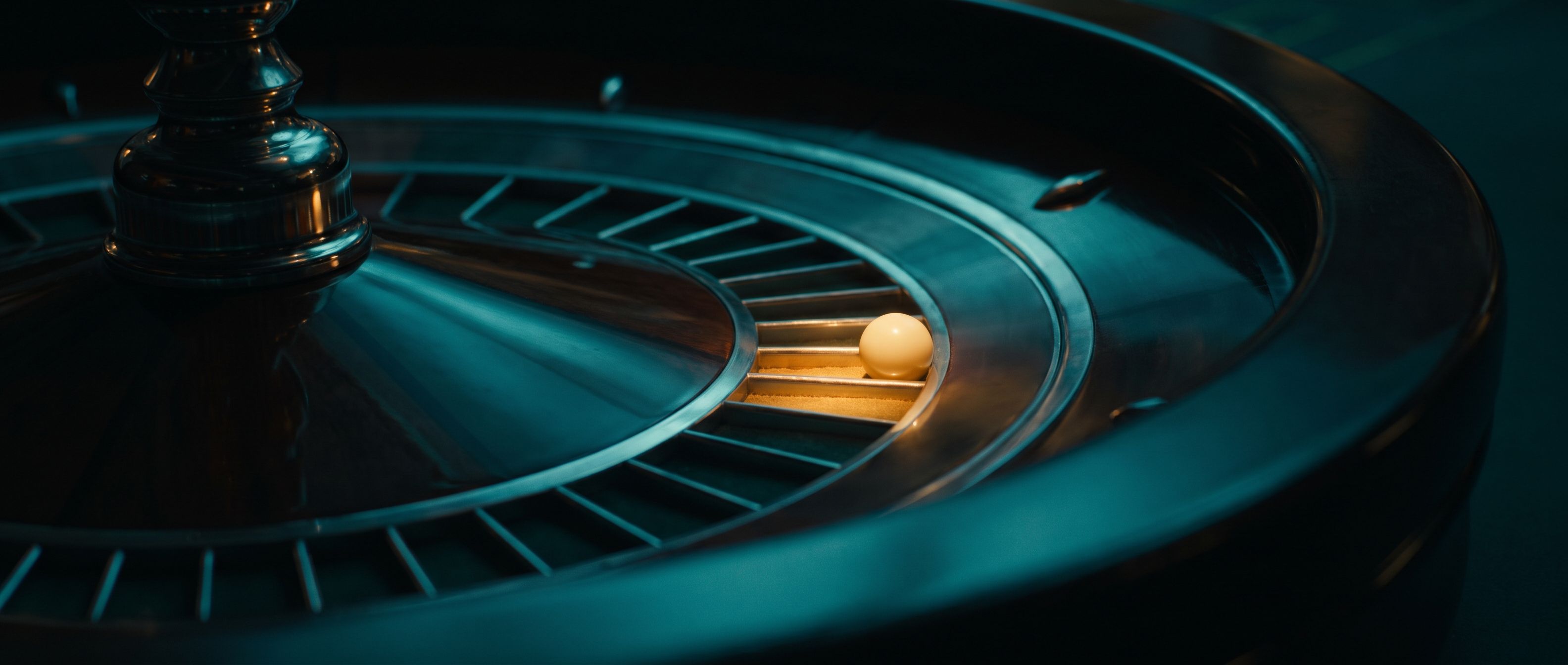 A roulette wheel in deep teal with one amber-lit pocket and the ball come to rest in it.
