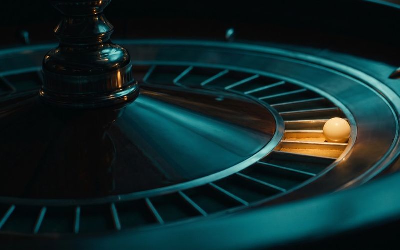 A roulette wheel in deep teal with one amber-lit pocket and the ball come to rest in it.