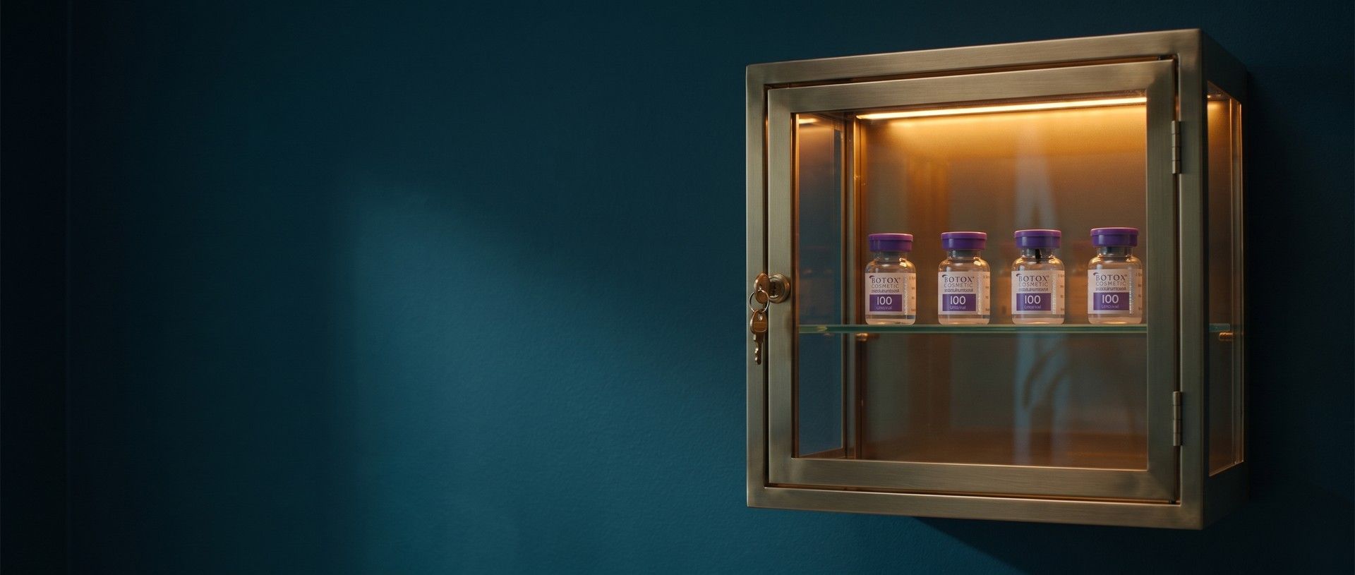 Four Botox Cosmetic vials lit warmly inside a brass-framed glass cabinet on a deep teal wall, a small brass key left in the lock