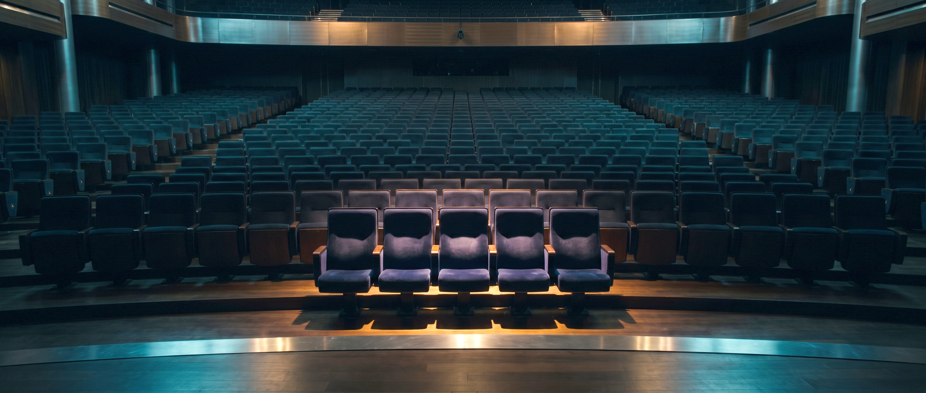 A vast dark auditorium of empty seats receding into shadow, with only a small cluster of seats near the front lit in warm amber, most of your buyers are not in the room yet.