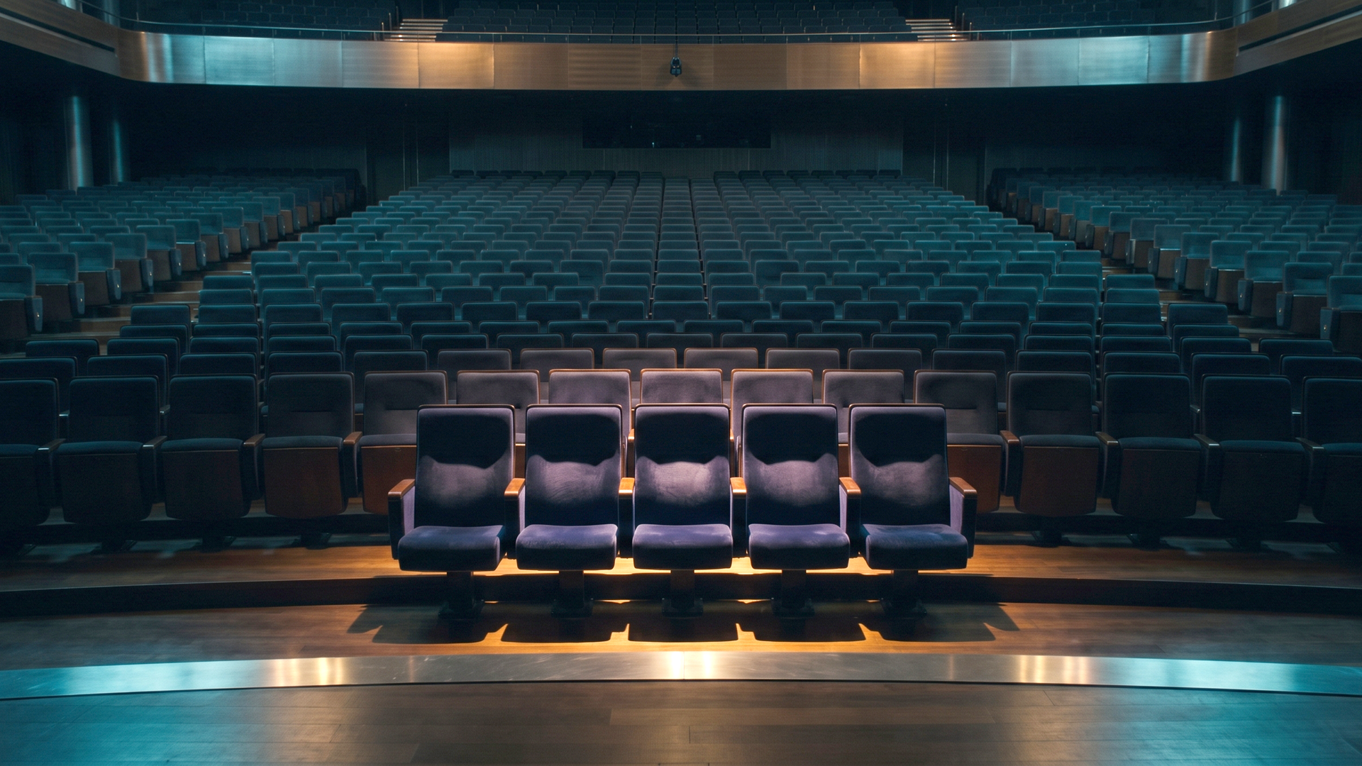 A vast dark auditorium of empty seats receding into shadow, with only a small cluster of seats near the front lit in warm amber, most of your buyers are not in the room yet.