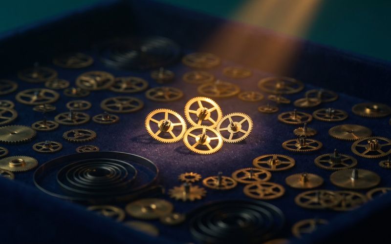 A watchmaker's tray of hundreds of tiny brass gears with four picked out in warm light