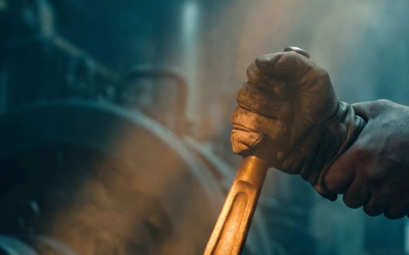 A gloved hand gripping a heavy amber-lit machine lever that is not moving