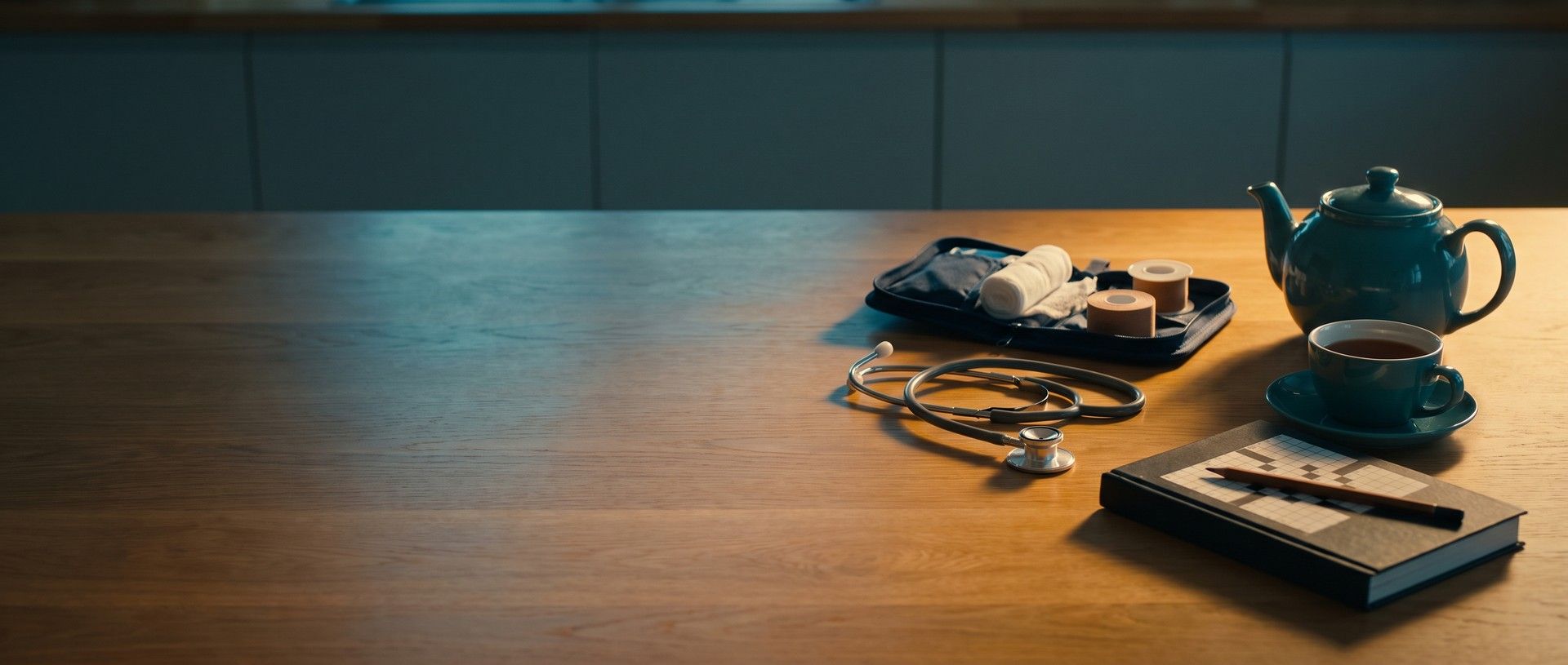 A stethoscope and an open wound-care kit on a sunlit wooden kitchen table beside a teal teapot, a cup of tea and a crossword book