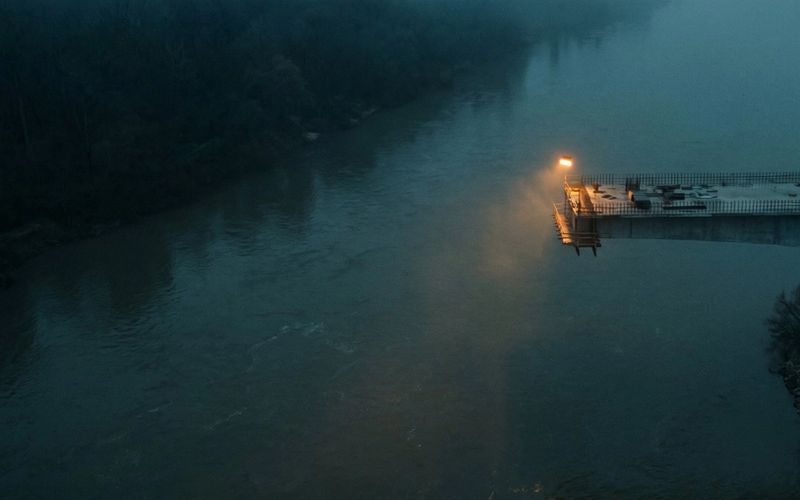 An unfinished road bridge stopping in mid-air over a river at dusk, with a single amber lamp at the cut end