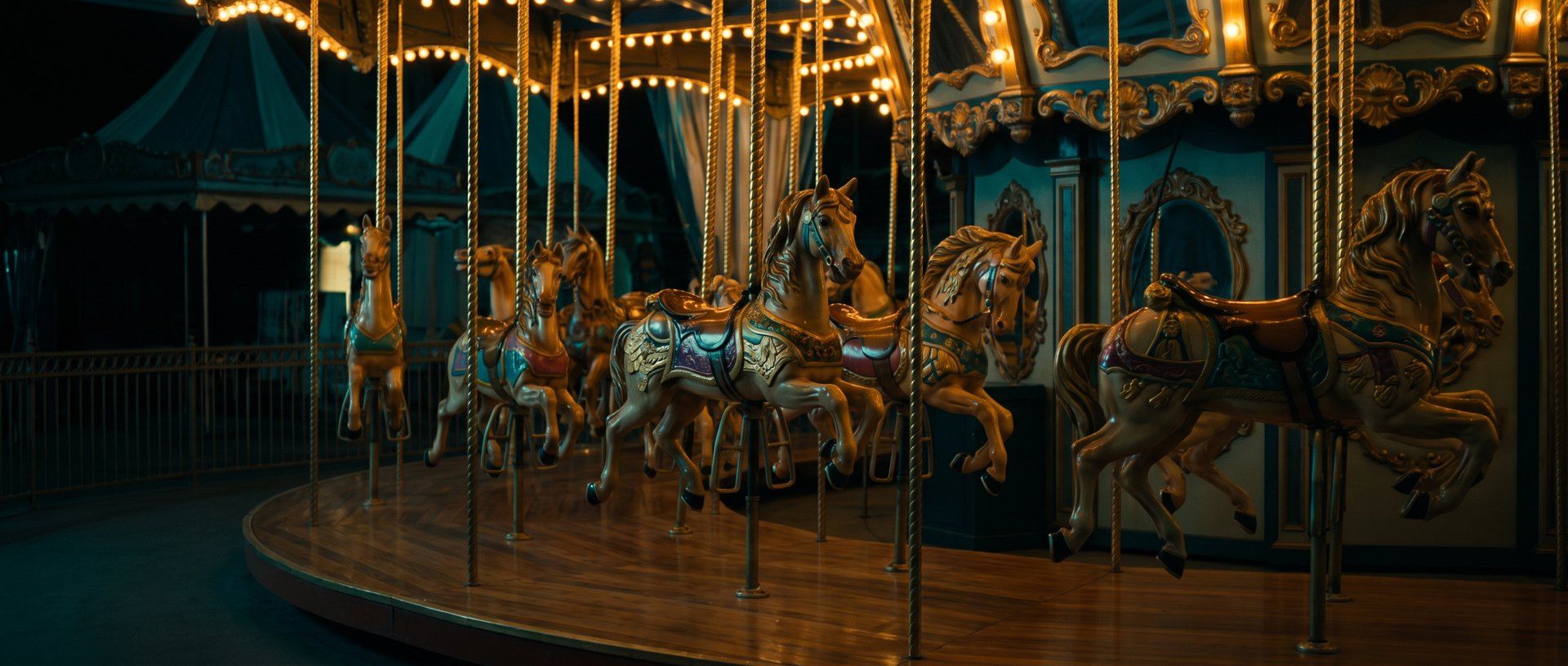 An ornate carousel at night, its carved horses lit in a row along the deck