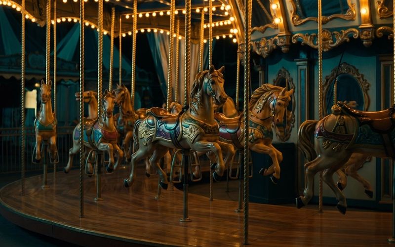 An ornate carousel at night, its carved horses lit in a row along the deck