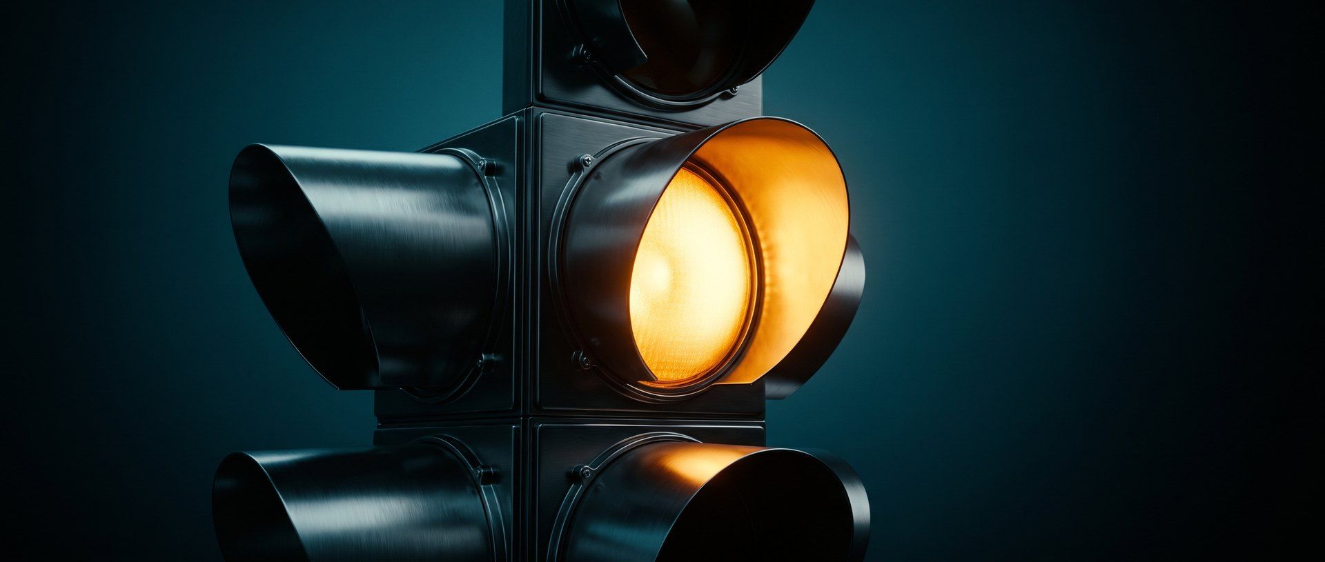 A traffic signal lit amber in close-up against a deep teal background, caught in the moment before it changes