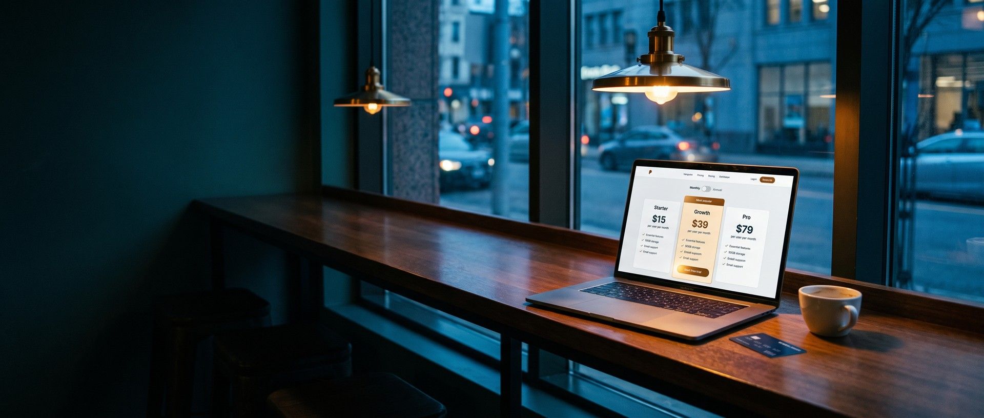 A laptop on a cafe counter at dusk open to a software pricing page with Starter, Growth and Pro plans, the Growth plan highlighted with a start free trial button, a business credit card and a coffee cup beside it