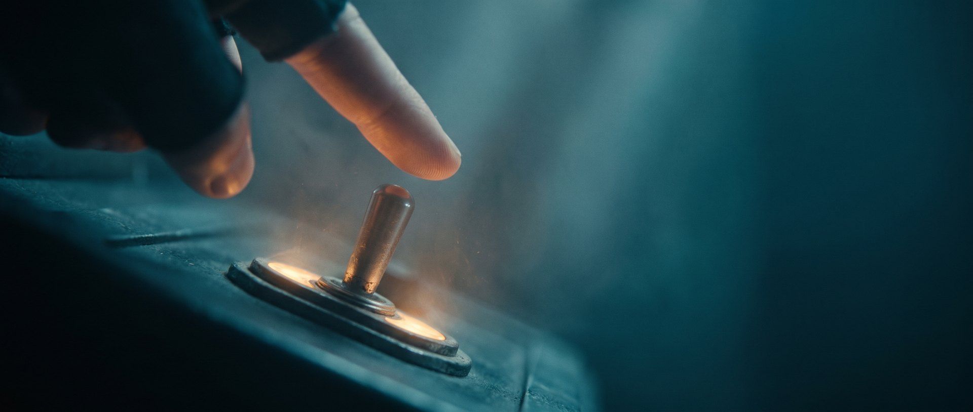 A fingertip about to flip a glowing brass toggle switch on a dark control panel, warm amber light around the switch, deep teal haze behind