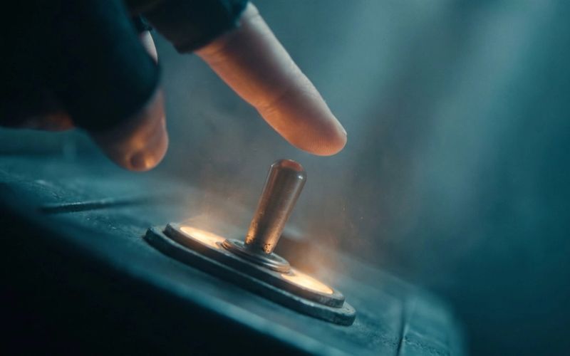 A fingertip about to flip a glowing brass toggle switch on a dark control panel, warm amber light around the switch, deep teal haze behind