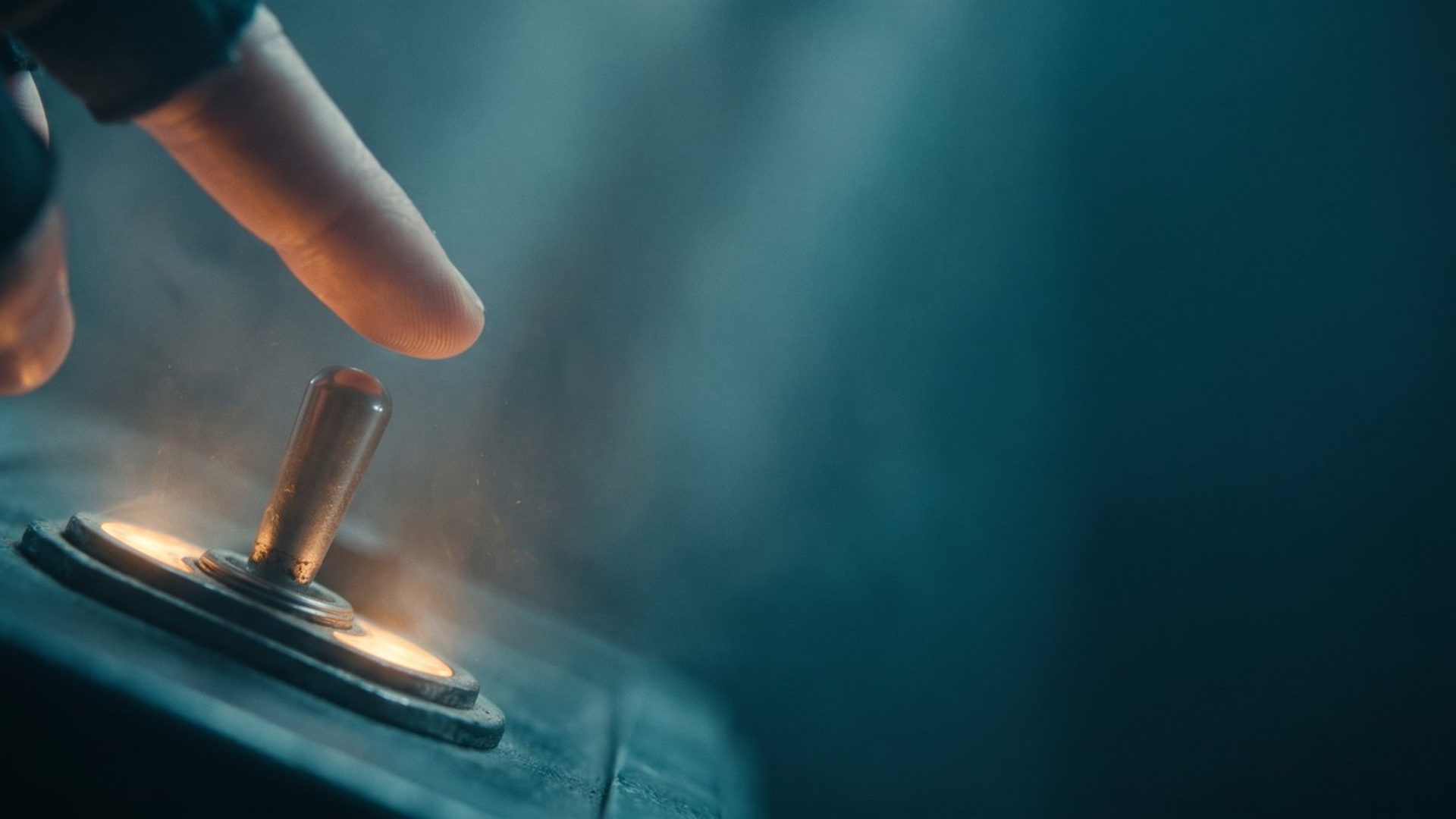 A fingertip about to flip a glowing brass toggle switch on a dark control panel, warm amber light around the switch, deep teal haze behind