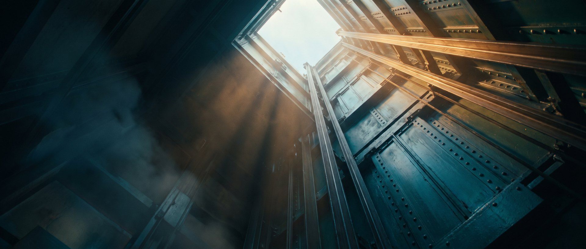 Looking straight up a deep industrial lift shaft that opens into bare sky at the top, with nothing capping it